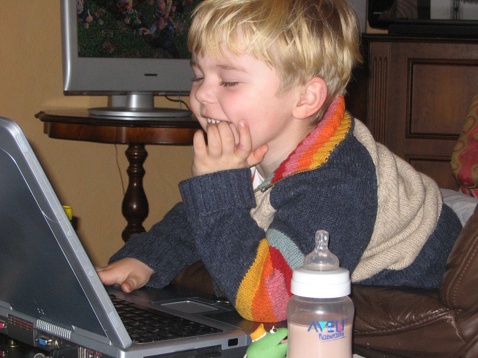 Picture of a young child smiling, looking at computer screen.
