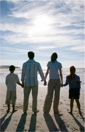 A picture of two adults and two children holding hands and looking out to the ocean from the beach.