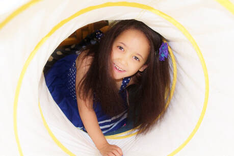 Image of smiling child crawling through play tunnel.