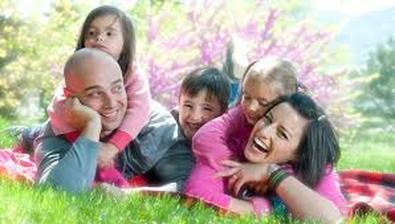 A picture of a smiling adult male and female lying on the ground with three children climbing on them.