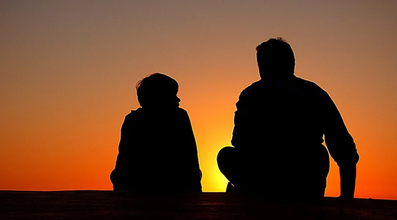 Silhouette of a child and a man sitting next to each other.