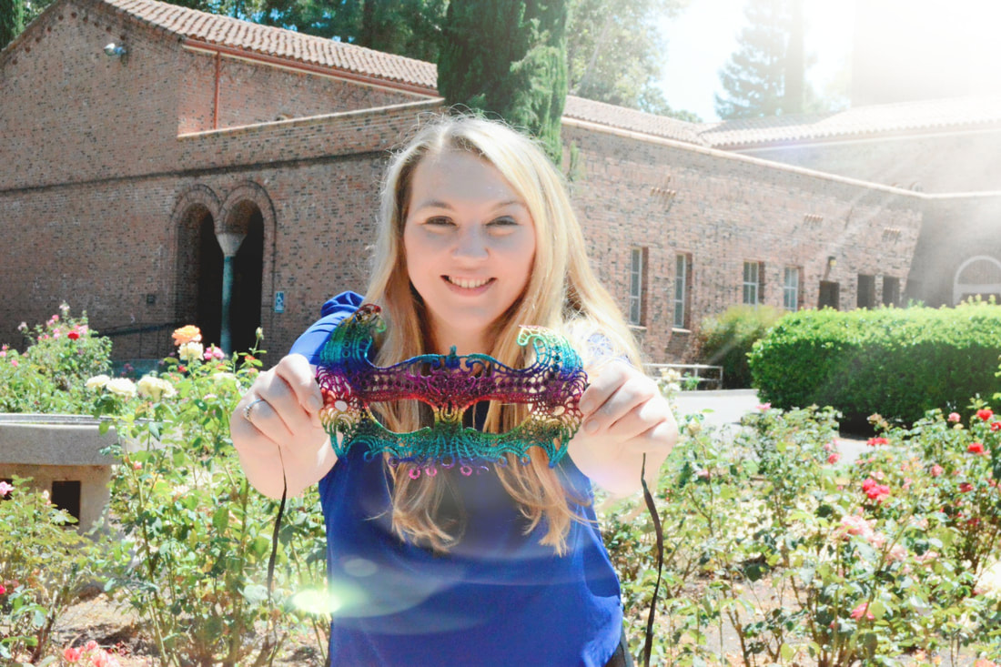 Picture of Tiffany Runge holding a rainbow mask in a garden, smiling.